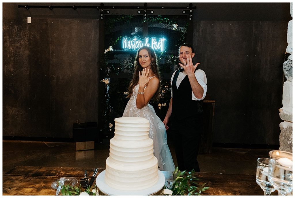 bride and groom in front of custom neon sign and cake